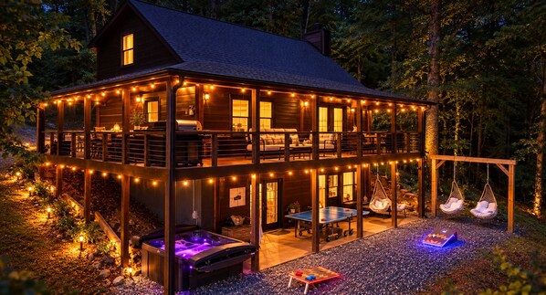 Eine zweistöckige Holzhütte mit einer Veranda, Sitzgelegenheiten im Freien und einem Whirlpool.