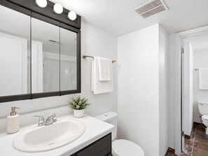 Ein Badezimmer mit weißem Waschbecken, Toilette, beleuchtetem Spiegel und Duschbereich.