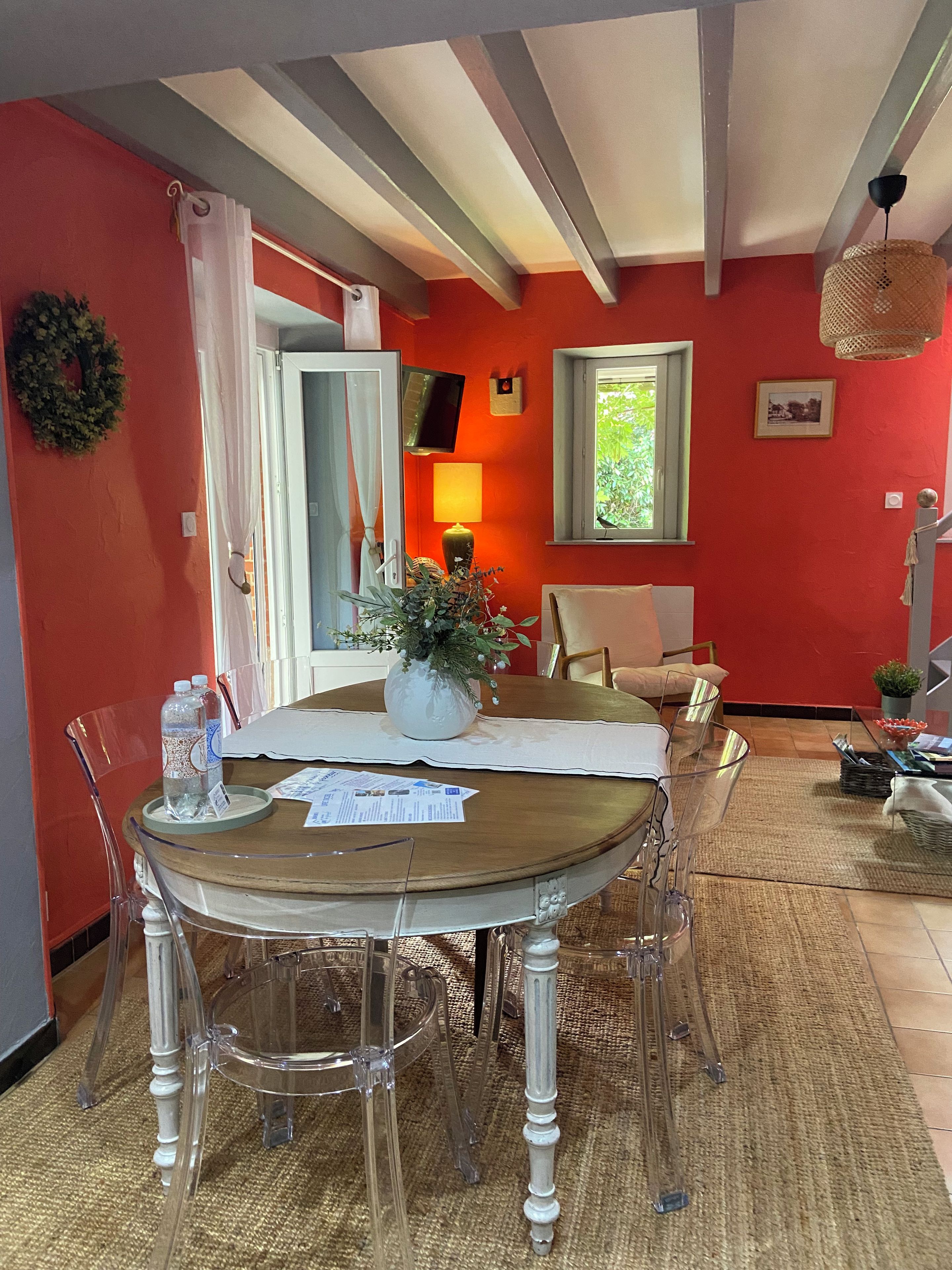 Un coin repas avec une table en bois, des chaises transparentes, un vase avec des fleurs et une lampe.