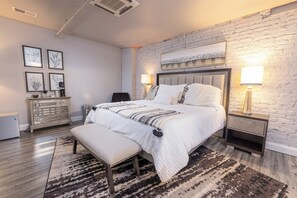 A modern bedroom with a large bed, a bench, a dresser, and a nightstand with lamps. - Cozy 1-bedroom hotel suite in beautiful Seneca with AC - ROOM 4 (Seneca)