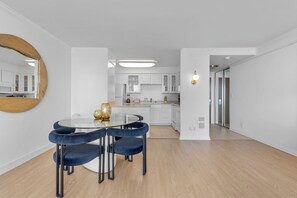 Una cocina moderna con armarios blancos, una mesa de comedor de vidrio con sillas azules y un espejo grande en la pared.