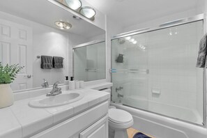 Un baño moderno con lavamanos blanco, inodoro y ducha con cerramiento de vidrio.