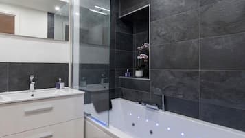 Un baño moderno con tocador blanco, cabina de ducha de vidrio y baldosas de piedra oscura.