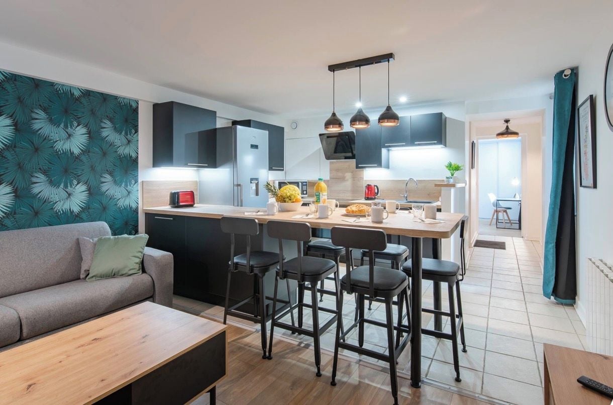 Una cocina moderna con una isla central, taburetes de bar y un área de comedor con sofá y mesa de centro.