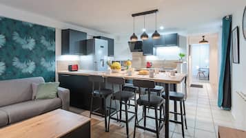 Una cocina moderna con una isla central, taburetes de bar y un área de comedor con sofá y mesa de centro.