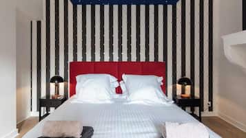 Una habitación de hotel con techo estrellado, cabecera roja, dos mesitas de noche con lámparas y una cama bien hecha con almohadas y toallas.