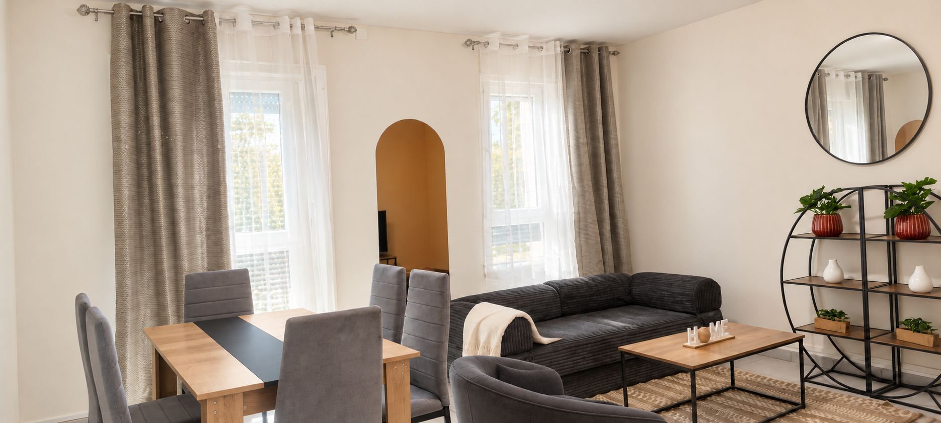 Ein modernes Wohnzimmer mit einer Couch, einem Esstisch mit Stühlen, einem Couchtisch und einem Bücherregal.