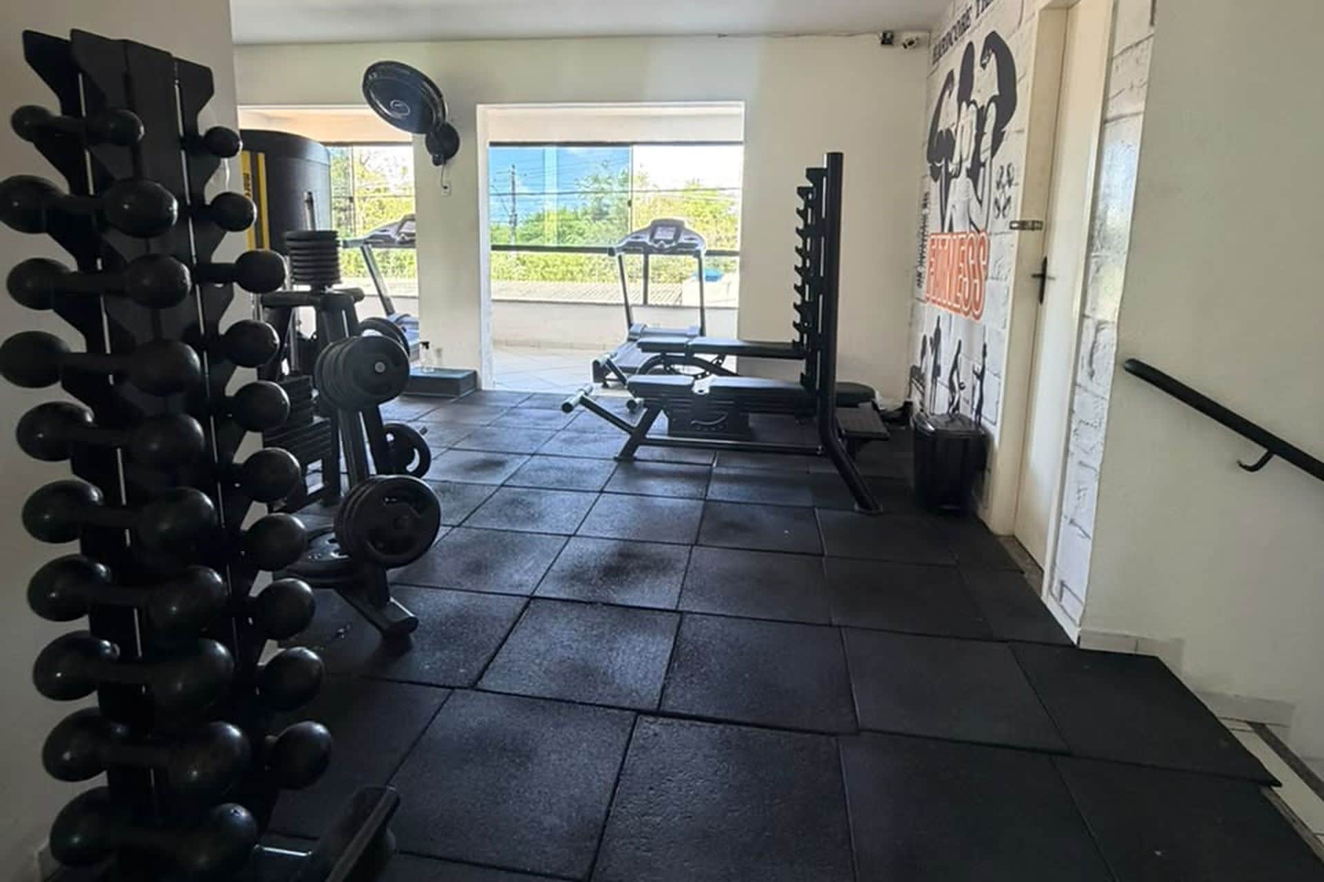 Et fitnessrum med styrketræningsudstyr, en bænkpres og en væg med en motiverende plakat.