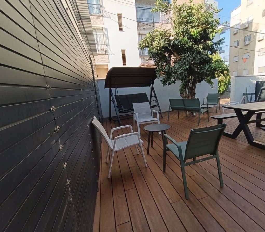 Un espace extérieur aménagé en terrasse, avec une plateforme en bois, un coin salon couvert et un arbre en pot.