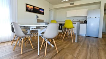 A modern kitchen with a dining area, wooden flooring, and a large window with curtains.