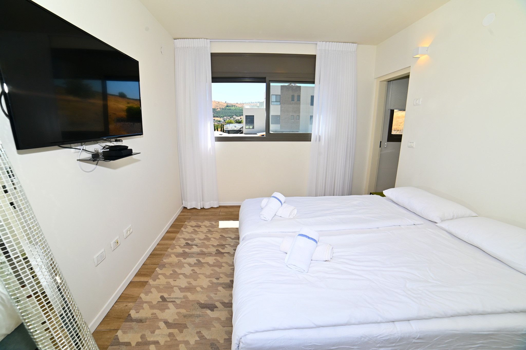 A hotel room with two beds, a television, and a window with curtains.