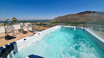 A hot tub on a balcony with a view of the sea and hills.