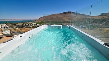 A hot tub with a clear view of the surrounding landscape, including a mountain and a body of water.