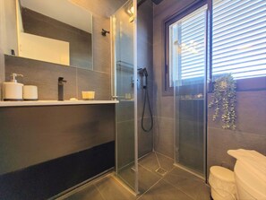 Een moderne badkamer met een douchecabine van glas, een toilet en een raam met zonwering.