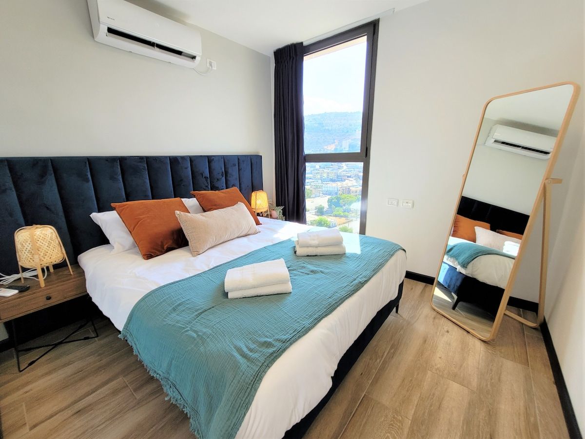 Een hotelkamer met een bed, nachtkastje, spiegel en een raam met uitzicht.