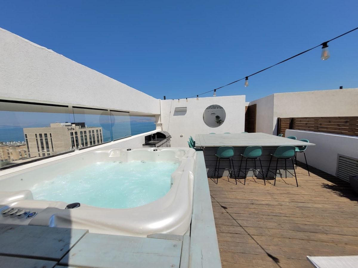 Een terras op het dak met een jacuzzi, een tafel met stoelen en een helder uitzicht op de stadshemel.