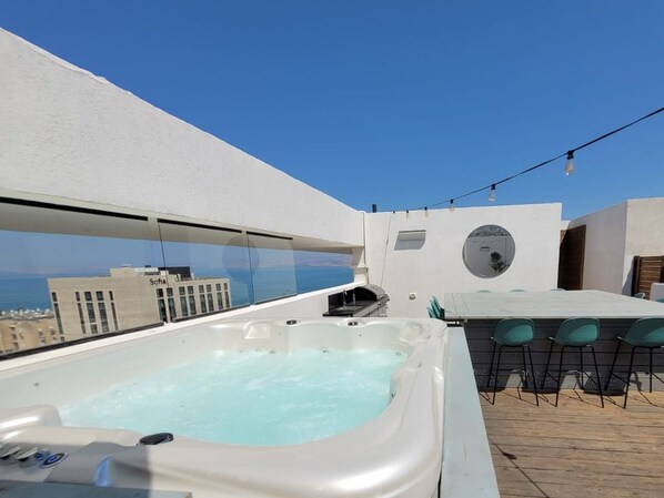 Een terras op het dak met een jacuzzi, buitenmeubels en een helder uitzicht op de stadshemel.