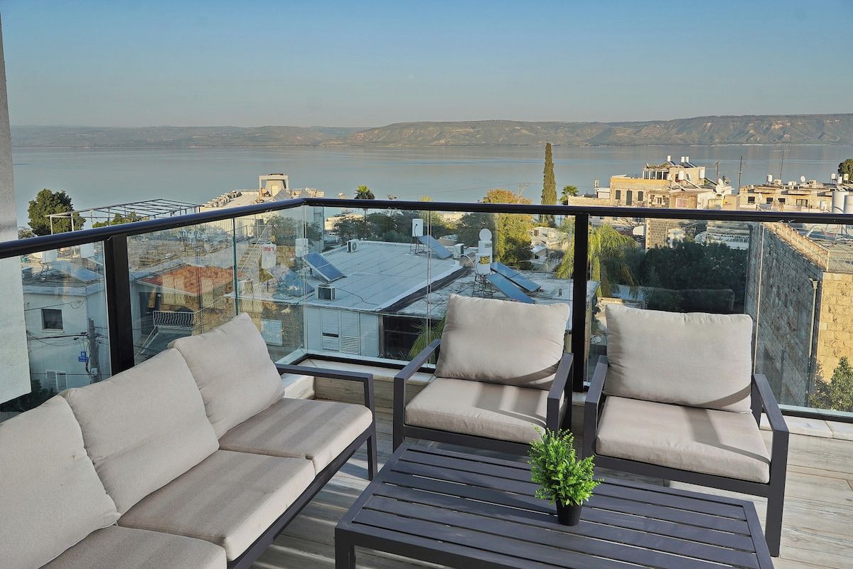 Een balkon met een bank, stoelen, een bijzettafeltje en een bloempot.