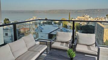 Een balkon met een bank, stoelen, een bijzettafeltje en een bloempot.