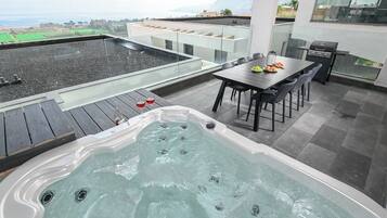 Une terrasse sur le toit équipée d’un jacuzzi, d’une table à manger, de chaises et d’un barbecue.