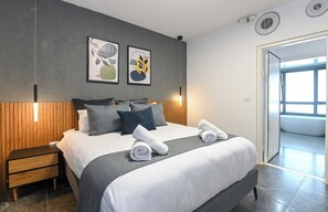 Une chambre d’hôtel moderne avec un grand lit, une tête de lit en bois et deux œuvres d’art abstraites accrochées au mur.