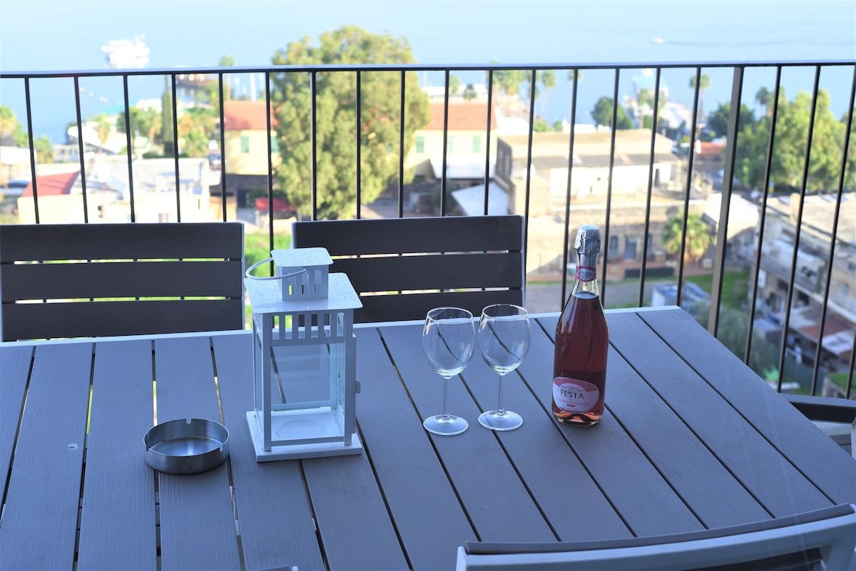 Een balkon met een tafel, twee stoelen, een fles wijn, twee wijnglazen en een kandelaar.