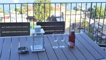 Een balkon met een tafel, twee stoelen, een fles wijn, twee wijnglazen en een kandelaar.