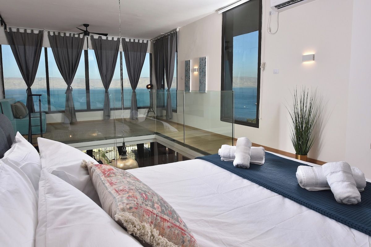 Een hotelkamer met een bed, een zithoek met uitzicht en een balkon met gordijnen.