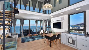 Een modern interieur met een eethoek, keuken en een groot raam met uitzicht op zee.