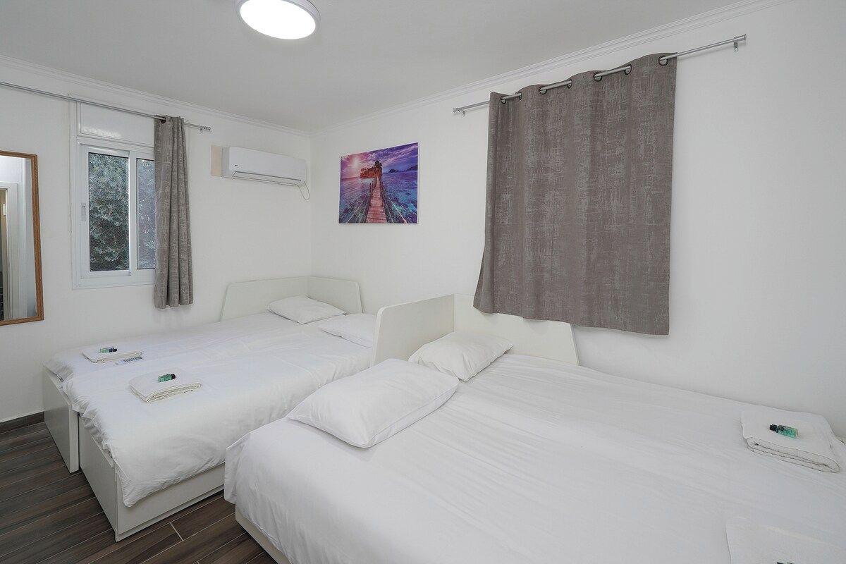Een hotelkamer met twee eenpersoonsbedden, een raam met gordijnen, een schilderij aan de muur en een airconditioning.
