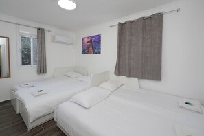Une chambre d’hôtel avec deux lits simples, une fenêtre avec des rideaux, un tableau au mur et un appareil de climatisation.