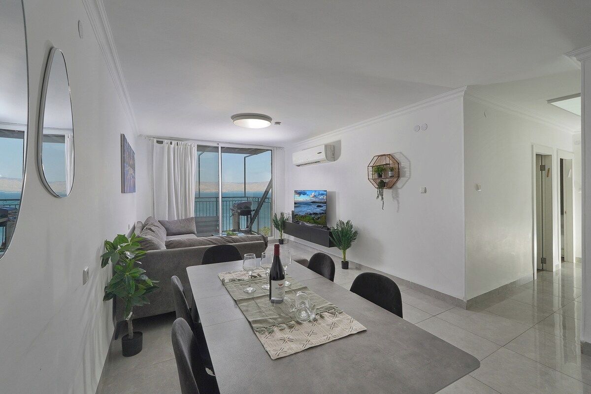 Een moderne woonkamer met een eethoek, grote ramen en uitzicht op zee.