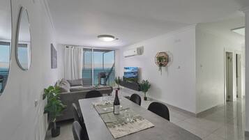 Een moderne woonkamer met een eethoek, grote ramen en uitzicht op zee.