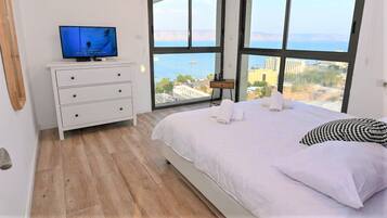 Een slaapkamer met een bed, een televisie op een dressoir en een groot raam met uitzicht op de stad.