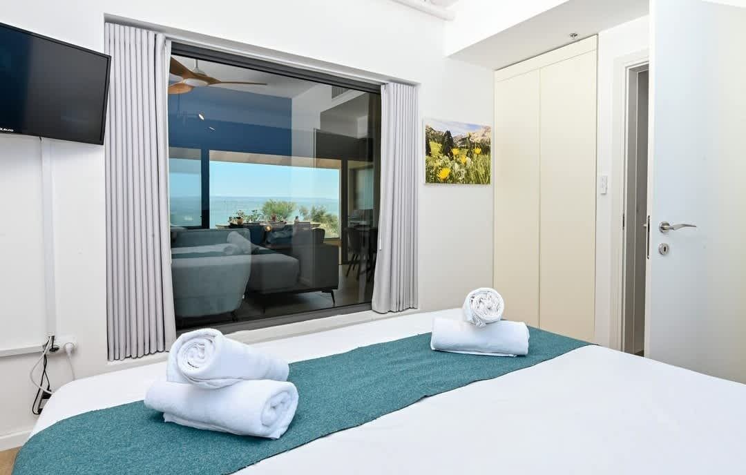 Habitación de hotel con cama, televisión, vista a través de un ventanal corredero y una puerta con manija.