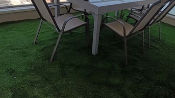 Een tafel met glazen blad en vier stoelen, omringd door een groen gazon, met uitzicht op een waterpartij en een veraf gelegen landschap.