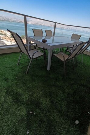 Een tafel met glazen blad en vier stoelen, omringd door een groen gazon, met uitzicht op een waterpartij en een veraf gelegen landschap.