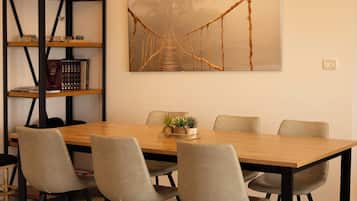 Een eethoek met een houten tafel, vier stoelen, een boekenkast en een schilderij van een brug.