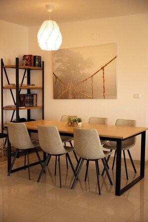 Een eethoek met een houten tafel, vier stoelen, een boekenkast en een schilderij van een brug.
