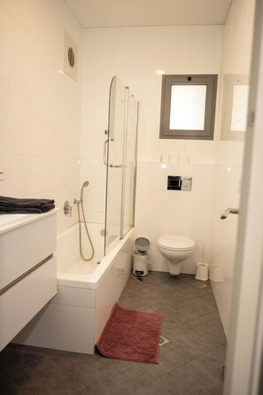 Een compacte badkamer met een douchecabine van glas, een wit toilet en een klein wastafeltje.