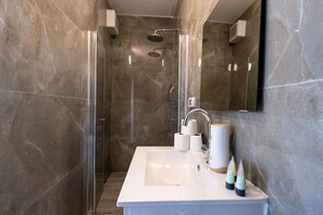Ein modernes Badezimmer mit einer gläsernen Duschkabine, einem weißen Waschbecken und einem Spiegel.