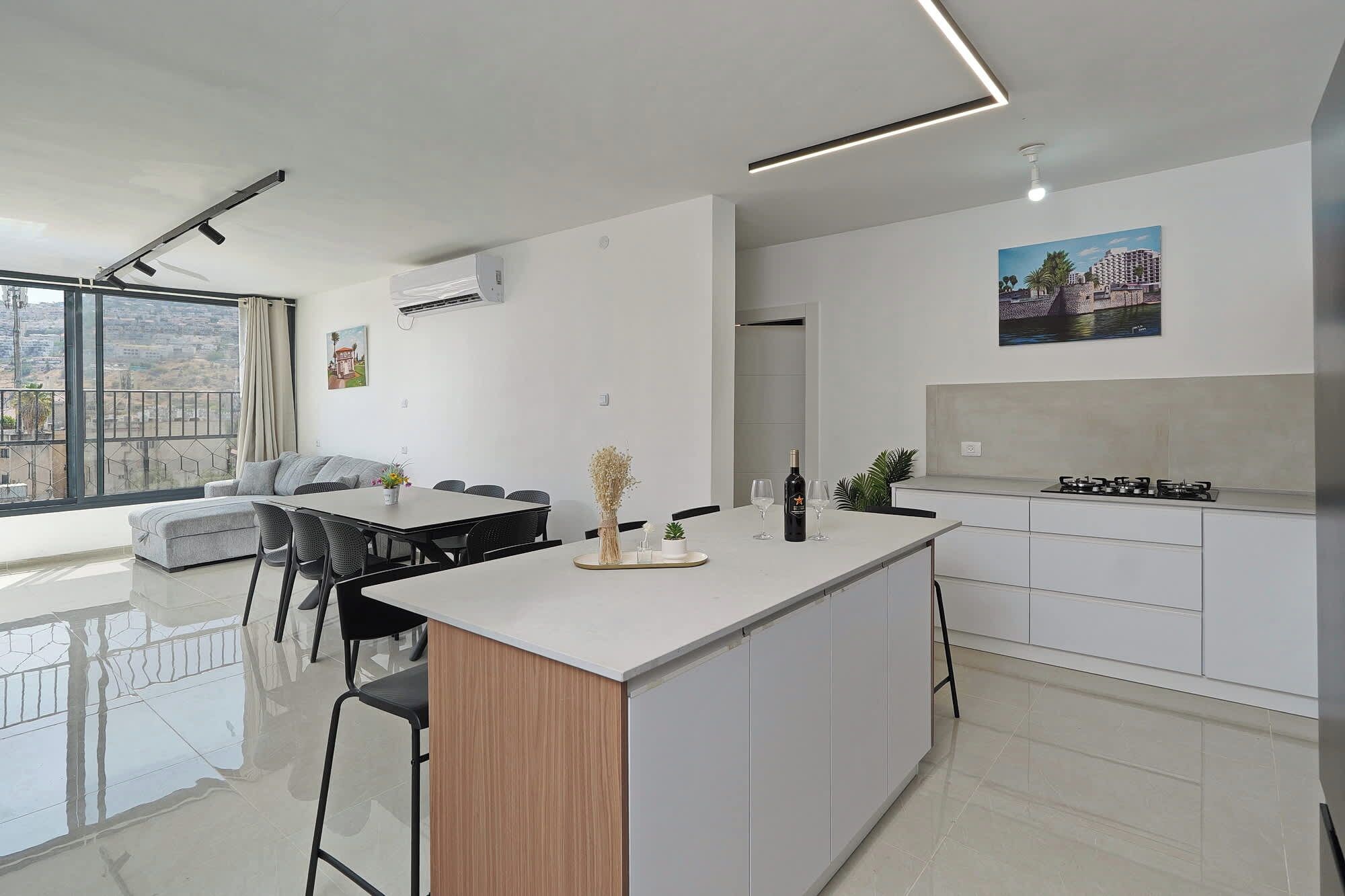 Een moderne keuken met een centraal eiland, een eethoek met stoelen en een groot raam met uitzicht op de stad.