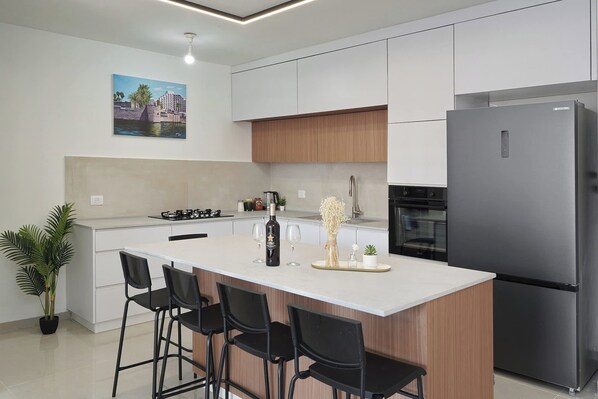 Een moderne keuken met een centraal eiland, barkrukken, een koelkast en een schilderij aan de muur.
