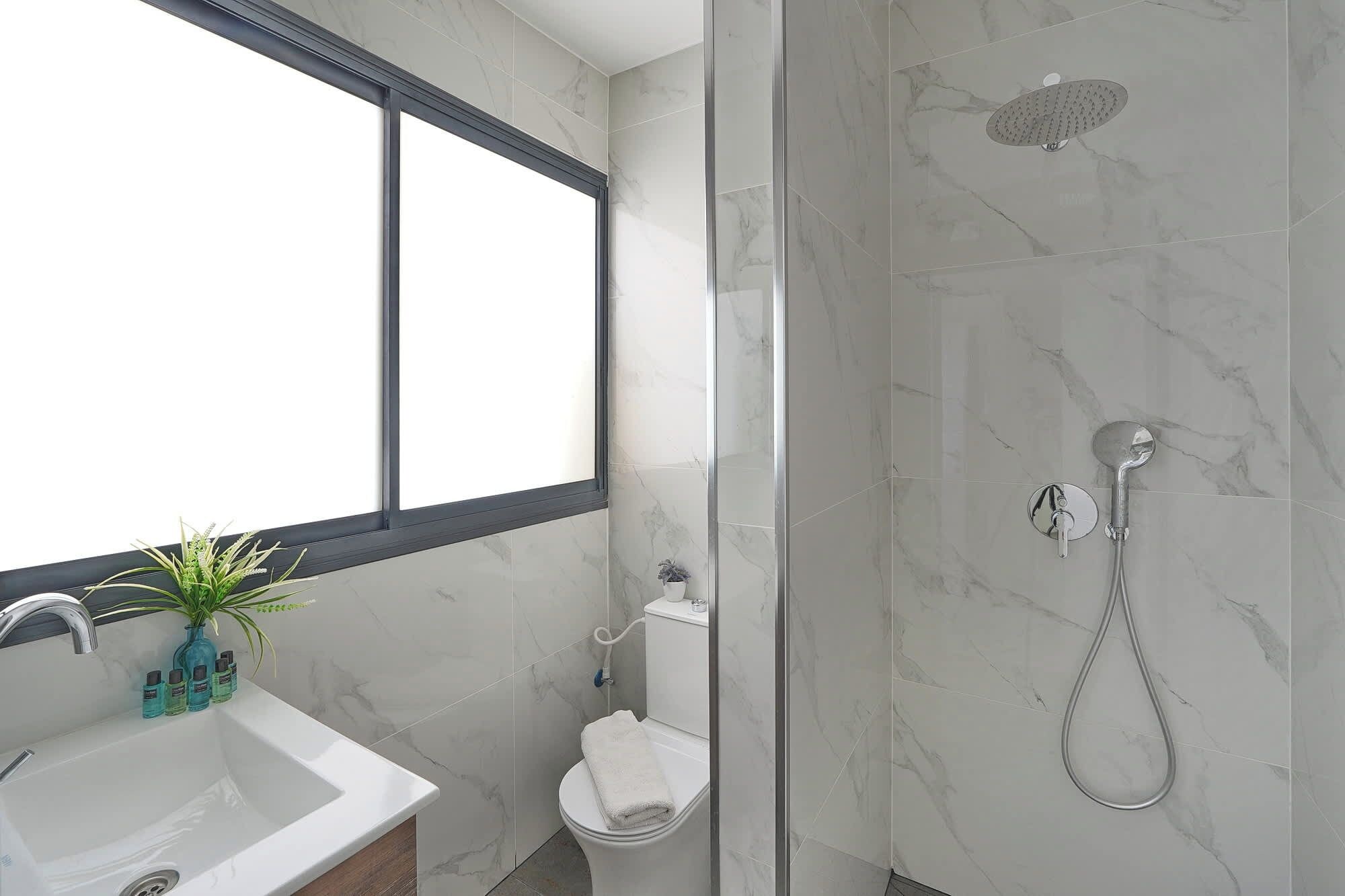Een badkamer met een douche, toilet, wastafel en een raam.