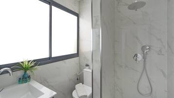 Een badkamer met een douche, toilet, wastafel en een raam.