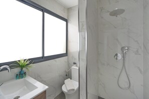 Een badkamer met een douche, toilet, wastafel en een raam.
