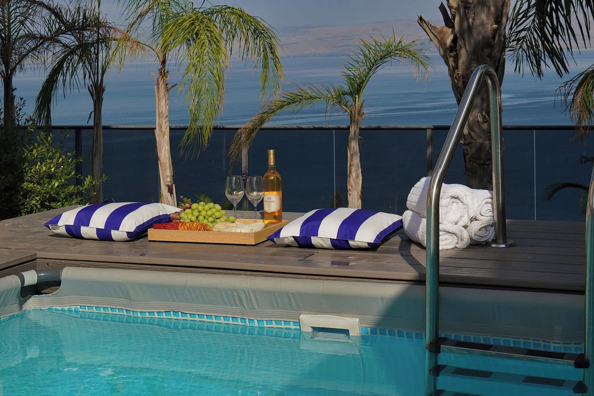 A poolside area with a pool, lounge chairs, a tray with food and drinks, and a view of the ocean.