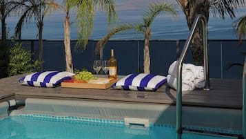 A poolside area with a pool, lounge chairs, a tray with food and drinks, and a view of the ocean.