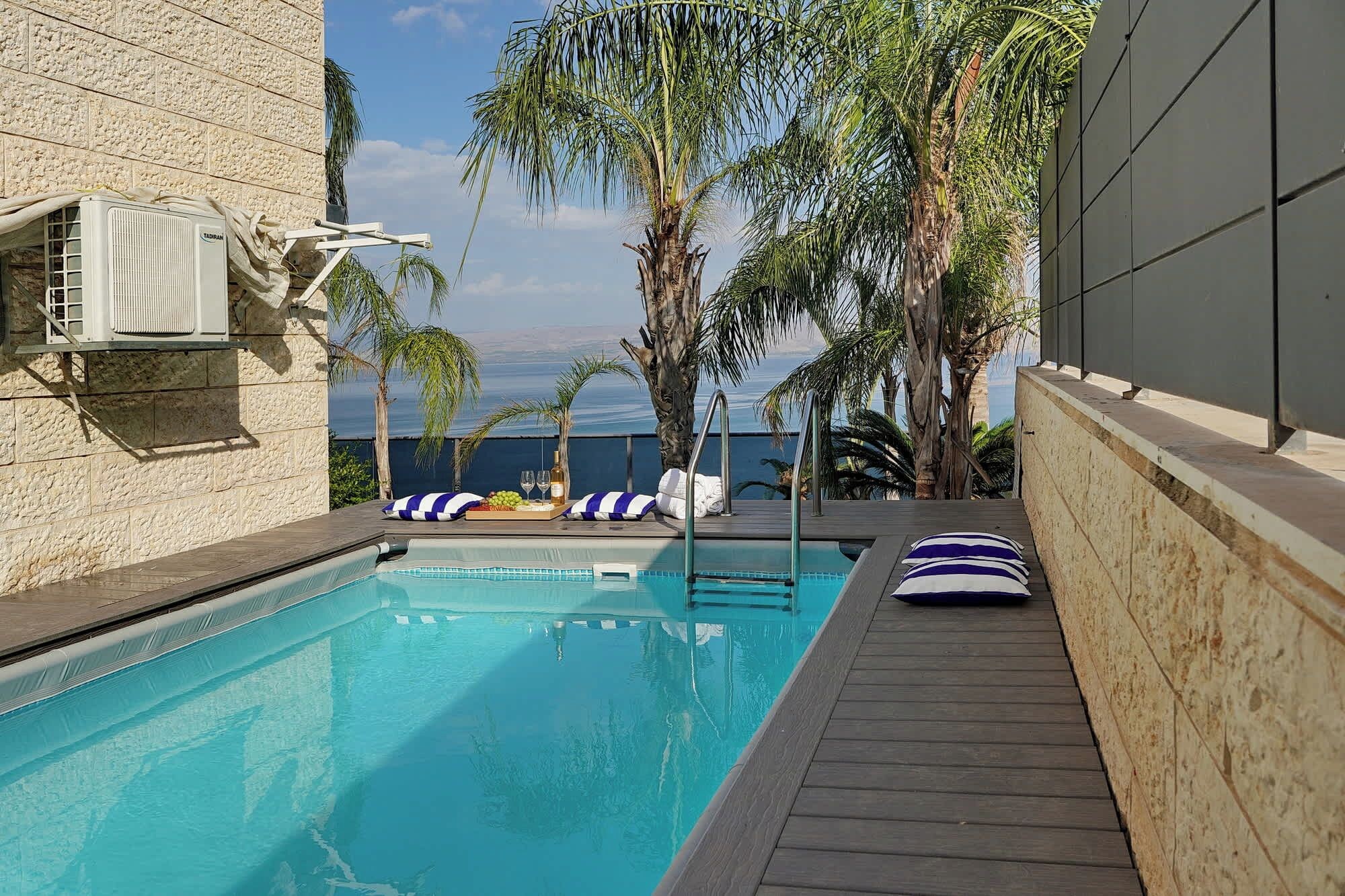 A swimming pool with a wooden deck, lounge chairs, and a view of the sea.