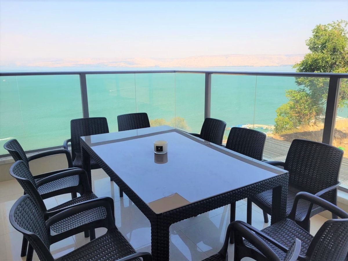 Een tafel met glazen blad en acht stoelen, een witte mok, en uitzicht op zee.